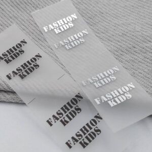 Дві прозорі етикетки з написом FASHION KIDS на тканині.