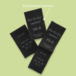Етикетки з чорної фарбованої бавовни з логотипом Blast Out Studio x upgrade, складом тканини та символами догляду.