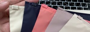 Hand holding a fan of matte plastic slider ziplock pouches in cream, navy blue, coral, and mauve with matching zip closures.