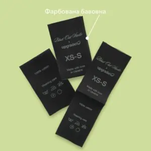 Етикетки з чорної фарбованої бавовни з логотипом Blast Out Studio x upgrade, складом тканини та символами догляду.